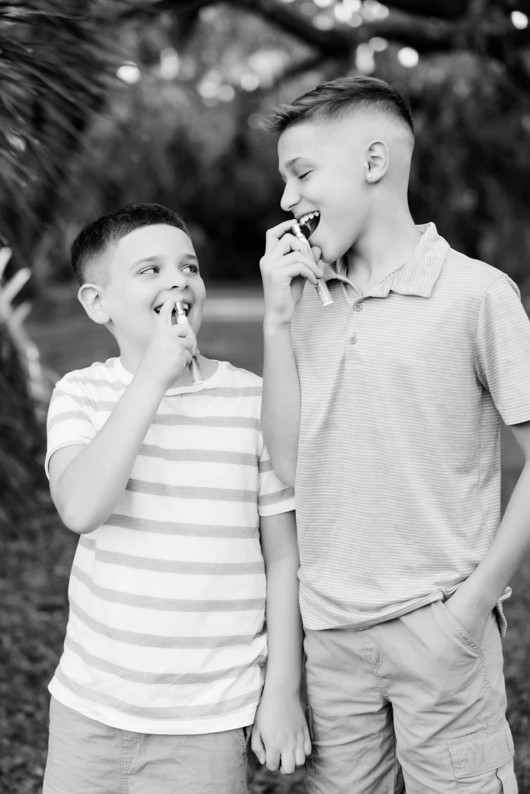 Two young brothers laughing outdoors while using NutraFi oral wellness sprays