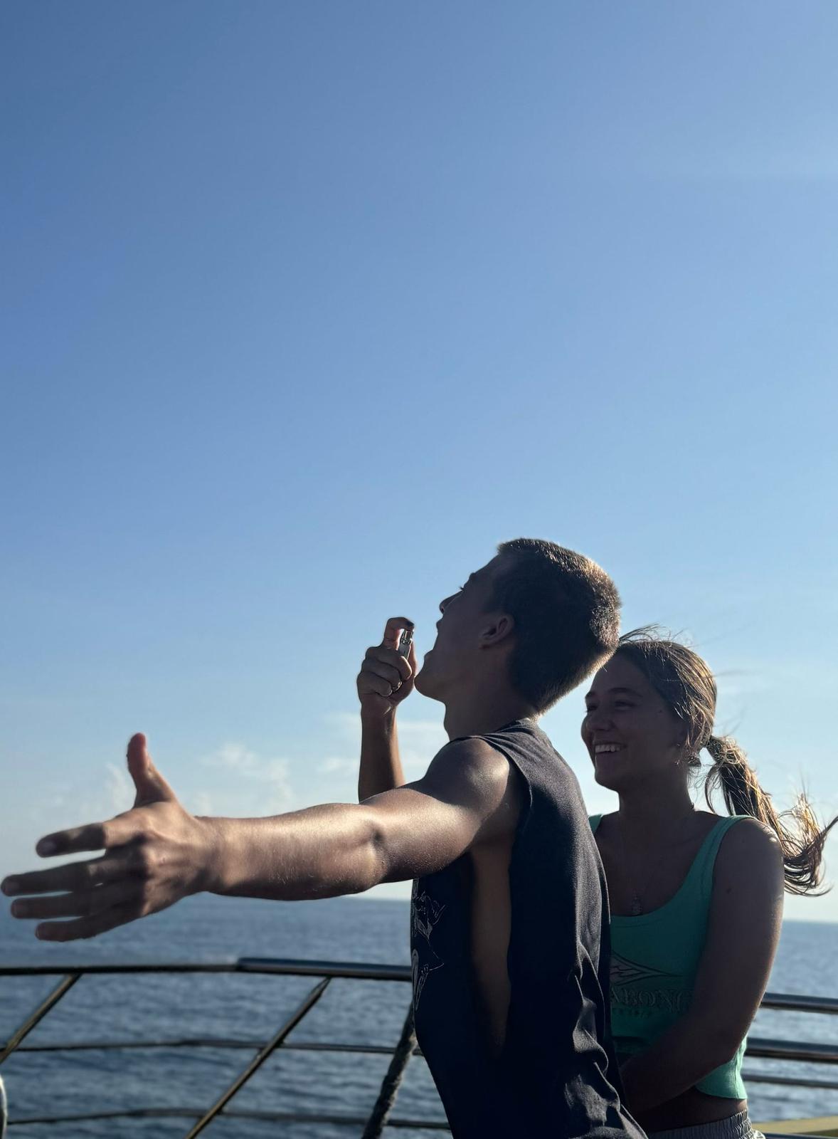 Young couple using NUTRAFi GLP-1 Relief oral spray outdoors by the ocean on a sunny day